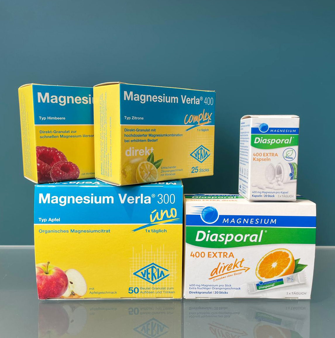 Produktfoto von fünf verschiedenen Magnesium-Präparaten der Marken Verla und Diasporal mit Fruchtmotiven vor blauem Hintergrund