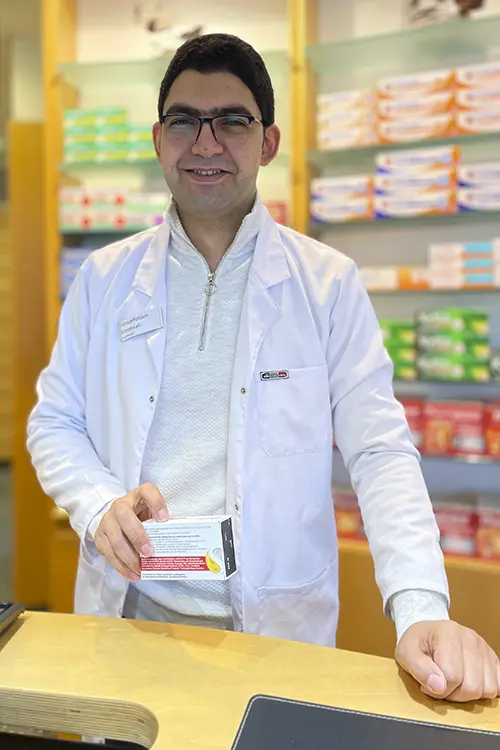 Fotouh Elmetwalli steht hinter dem Tresen, hält ein Produkt in der Hand und lächelt in die Kamera.