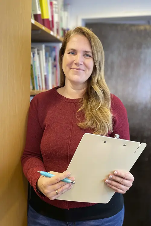 Juliane Reuscher hält ein Klemmbrett und einen Kugelschreiber in der Hand und lächelt in die Kamera.